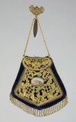 Black silk velveteen chatelaine bag in pentagon shape. Finished with gold metal bead twisted and looped fringe. Front embellished with gold metal filigree design, centered with a medallion featuring a depiction of a neoclassical building with ten figures in foreground. Opens at top with hinged filigree flap featuring a turquoise studded rose at center. Purple…
