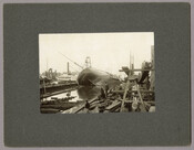 A group of people survey the steamship "Hudson," which lays on its side, at the shipyards in Baltimore, Maryland. The steamship "Kitty Knight" is also visible in the background. The “Hudson” was a 1900-ton steamer owned by Baltimore’s Merchants & Miners Steamship Company. While being repaired in the William Skinner & Sons Shipbuilding and Drydock…