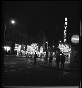 Evening street view of "The Block," the 400 block of East Baltimore Street in Baltimore, Maryland, known for its nightlife and adult entertainment venues. A sign for "Gayety" is visible along with other advertisements and signs.