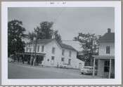 Side view of a store with two figures standing outside in Still Pond, Maryland. Located next to the William Medders & Co. store, which can be partially seen to the right, this building was originally constructed by George Washington Covington. Elmer Kennard Jones operated the store from 1934 to 1969.
