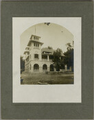 A side view of the Excursion house at the Tolchester Beach Amusement Park in Tolchester, Maryland. Two figures sit on a low ledge of the building. This Kent County park consisted of a bathing beach, amusement park, racetrack, and hotel, and was in operation from 1877 to 1962. It was a popular vacation destination for…