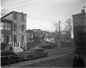 View of two boys standing beside row houses and parked cars on an unidentified alley street in Baltimore, Maryland. Clothes lines and yards of homes on a nearby block are visible in the background.