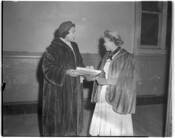 Marian Anderson (1897-1993), at left, talking to Emma Bright. Both women are wearing hats and fur jackets, and Anderson holds a wrapped present in her hands.