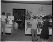 Customers inside a delicatessen or grocery. Several people are in front of displays and an employee is visible in a back room.