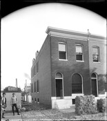 A view of the newly-constructed rowhome at 2300 Ashland Avenue in East Baltimore, Maryland. Two people stand near the cobblestone alley at the side of the building and a portion of the rowhome located at 2302 is also visible.